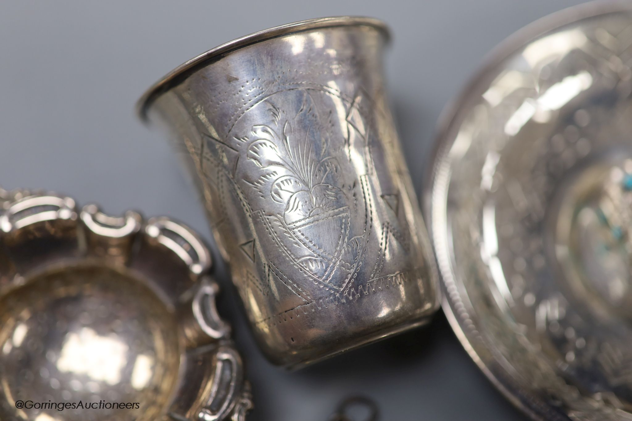 A late 19th century Russian engraved 84 zolotnik beaker, 1893, 63mm, a similar saucer, 1886, three assorted similar spoons, a white metal thimble and pendant and a German 835 tea strainer